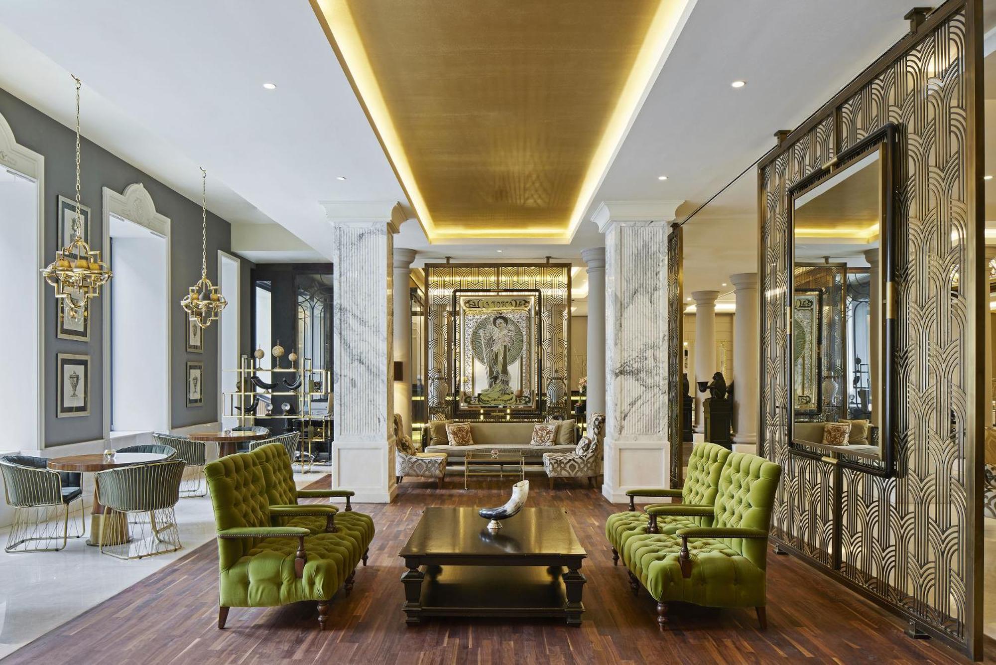 柏林御林广场泰坦尼克酒店 外观 照片 The photo depicts a stylish and elegant interior space, likely a lobby or lounge area. It features tall ceilings with sophisticated lighting and a modern design aesthetic. There are two vibrant green chairs positioned around a dark wooden coffee tabl