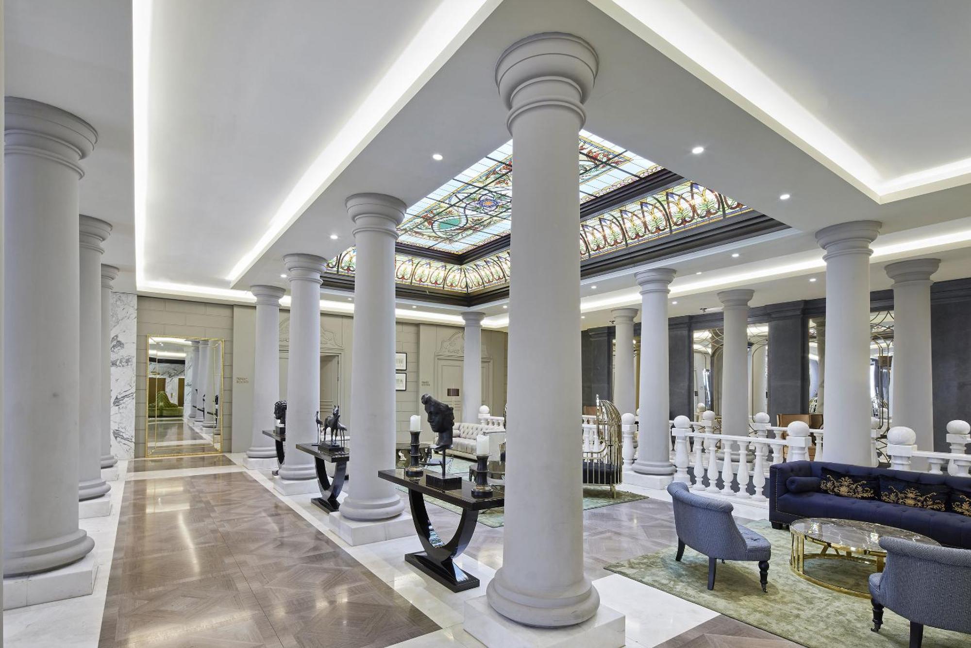 柏林御林广场泰坦尼克酒店 外观 照片 The photo depicts an elegant interior space, likely a lobby or a grand hall. It features tall, decorative columns that line the area, creating a sense of grandeur. The ceiling is adorned with intricate designs and stained glass, allowing light to fil
