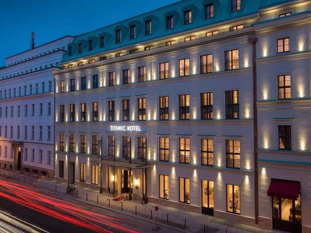 柏林御林广场泰坦尼克酒店 外观 照片 The photo shows the exterior of a hotel building, specifically named "Titanic Hotel." It appears to be taken during the evening, as the sky has a twilight blue hue. The hotel features a modern architectural design with large, illuminated windows that